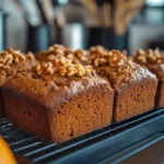 Freshly baked pumpkin bread mix loaves topped with crunchy walnuts cooling on a wire rack, with a blurred kitchen background and small pumpkins adding a cozy autumn feel.